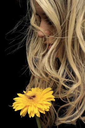 Close up shot of a pretty blonde girl holding a single yellow flower